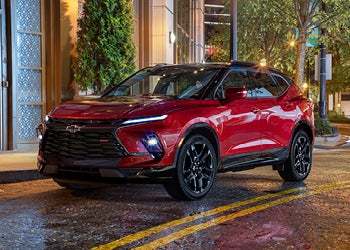 Red Chevrolet SUV parked on a city street at night with lights reflecting on wet pavement.